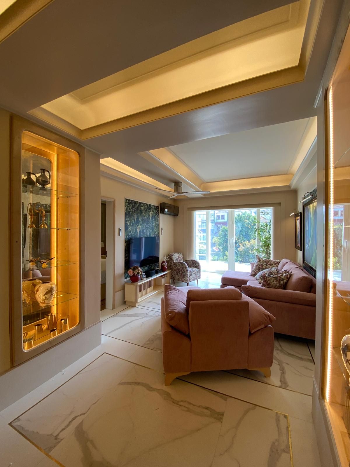 A spacious living room with a large flat-screen TV, a sofa set, and a decorative glass cabinet.