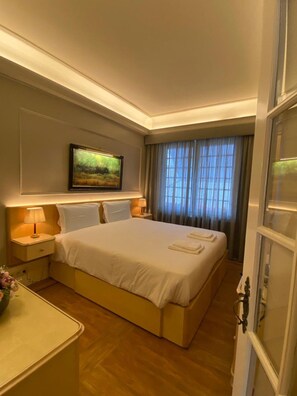 A hotel room with a large bed, a nightstand with a lamp, a painting on the wall, and a window with curtains. - Poirot Oporto Apartment (Porto)