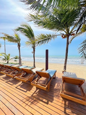 A wooden deck with lounge chairs and a view of the ocean.