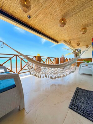 A hammock under a wooden ceiling with a view of the ocean.