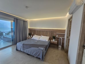 A modern hotel room with a large bed, bedside tables, a nightstand, a potted plant, and a sliding glass door leading to an outdoor area.