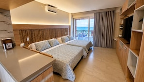 A hotel room with a bed, bedside table, TV, and a balcony with curtains.