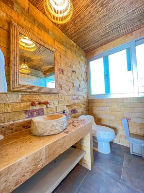 A bathroom with a stone wall, a wooden vanity, a large mirror, and a toilet.