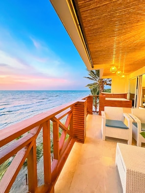 A balcony with a wooden railing overlooking the sea, furnished with wicker chairs and a small table.