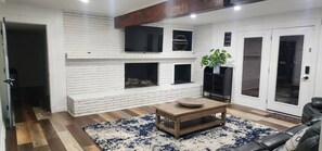 Ein Wohnzimmer mit Kamin, Flachbildfernseher und schwarzem Ledersofa.