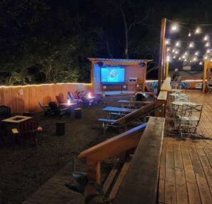 An outdoor patio area with a wooden deck, seating arrangements, and a small screen displaying a video. - Nashville Getaway - Sleeps 8 - 9 Min to Broadway (Nashville)