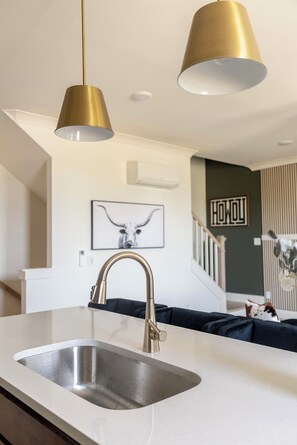 Une cuisine moderne dotée d’un évier en acier inoxydable, de luminaires suspendus dorés et d’un climatiseur fixé au mur.