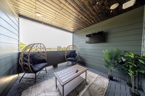 Ein moderner Außenbereich mit Holzdecke, zwei gepolsterten Stühlen, einer Bank und einem an der Wand befestigten Flachbildfernseher.