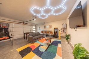 Ein Wohnzimmer mit einer Couch, einem Kicker, einem bunten Teppich und einer Deckenleuchte.
