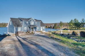 A two-story house with a front porch, a driveway leading to the entrance, and a body of water in the background. - Scenic Lake Getaway: Private Sauna & Beach Access (Greenfield Township)