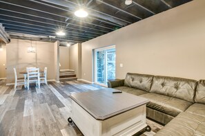 A spacious living area with a sofa, a dining table with chairs, and a staircase leading to a balcony. - Scenic Lake Getaway: Private Sauna & Beach Access (Greenfield Township)