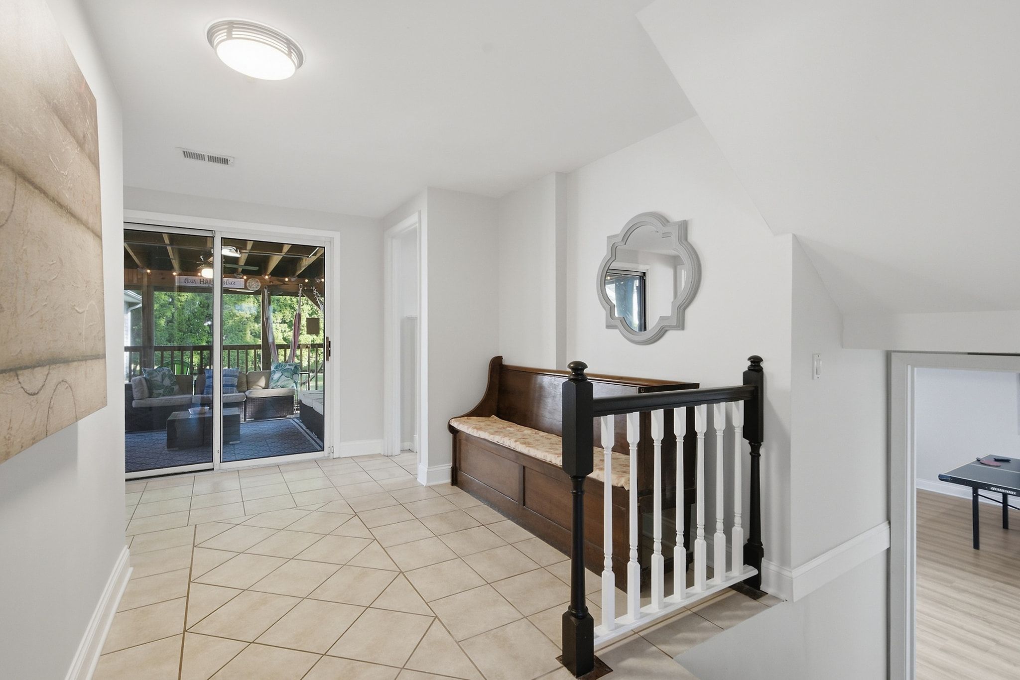 A spacious hallway with a wooden bench, a mirror on the wall, and a view into a patio area.