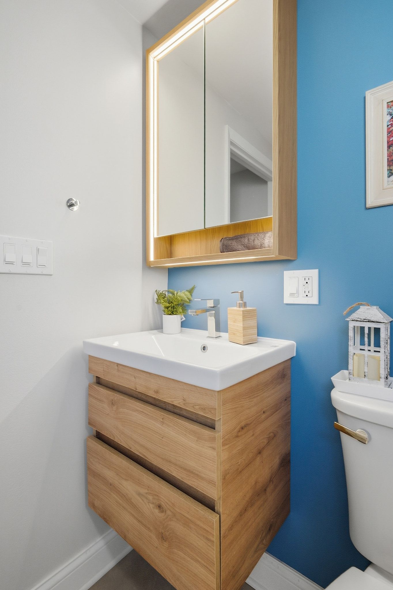 Ein Badezimmer mit einem Holzkosmetikschrank, einem weißen Waschbecken, einem Spiegel und einer blauen Akzentwand.