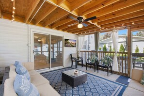 Un patio exterior con un ventilador de techo, una puerta de vidrio que da a un área techada, y un conjunto de mesa y sillas.