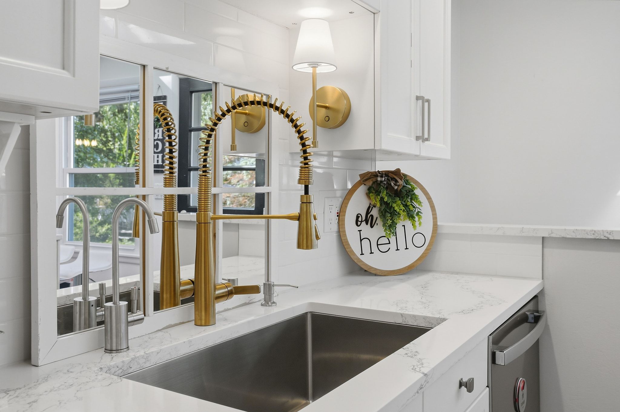 Een moderne keuken met een gouden kraan, een wandlamp en een bordje met de tekst 'hello'.