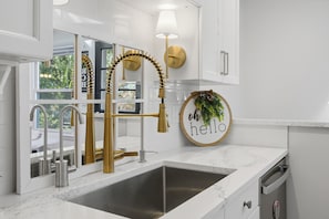 A modern kitchen with a gold faucet, a wall-mounted lamp, and a 'hello' sign.