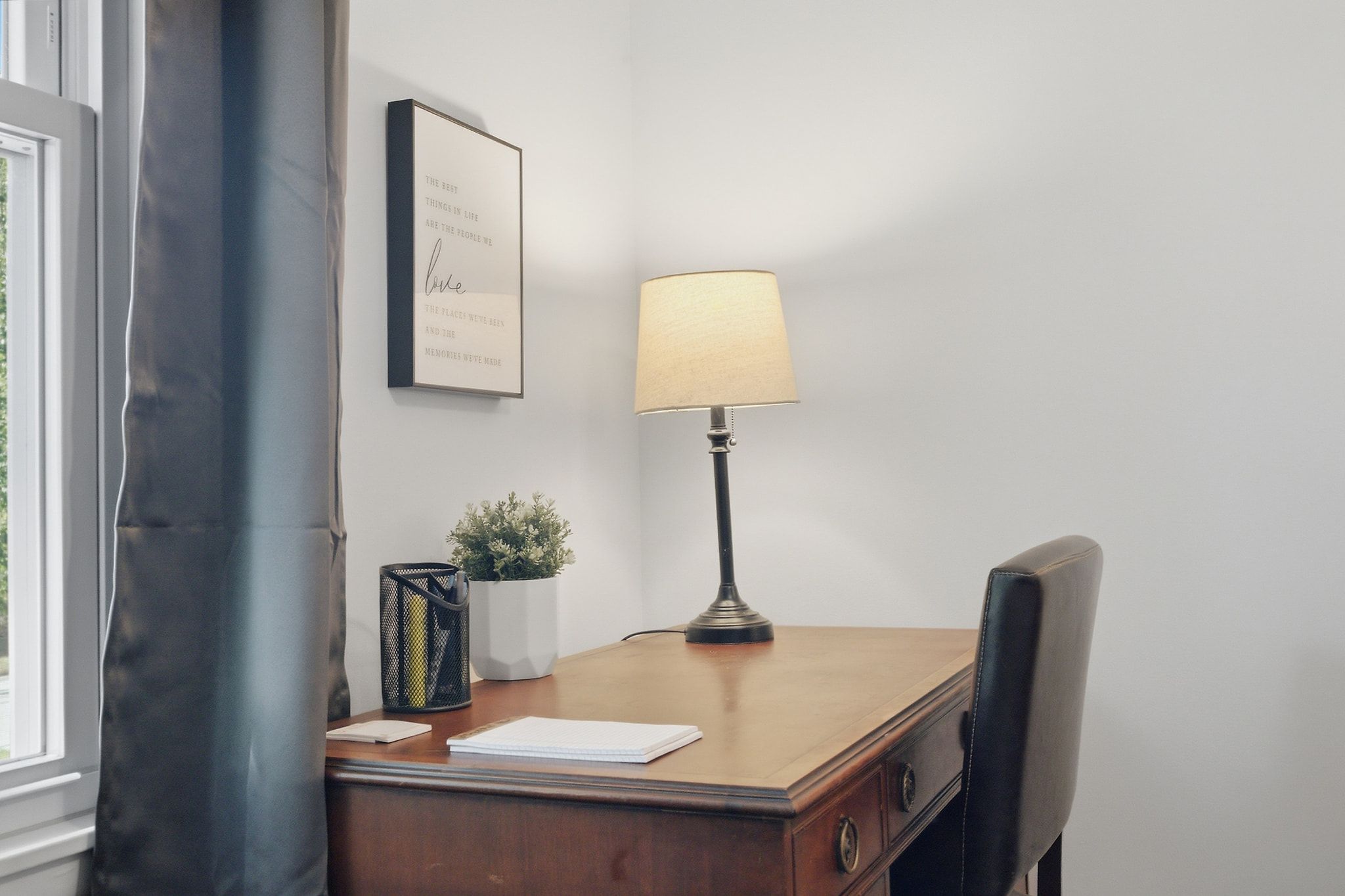 A desk with a lamp, a framed quote, a potted plant, and a chair.