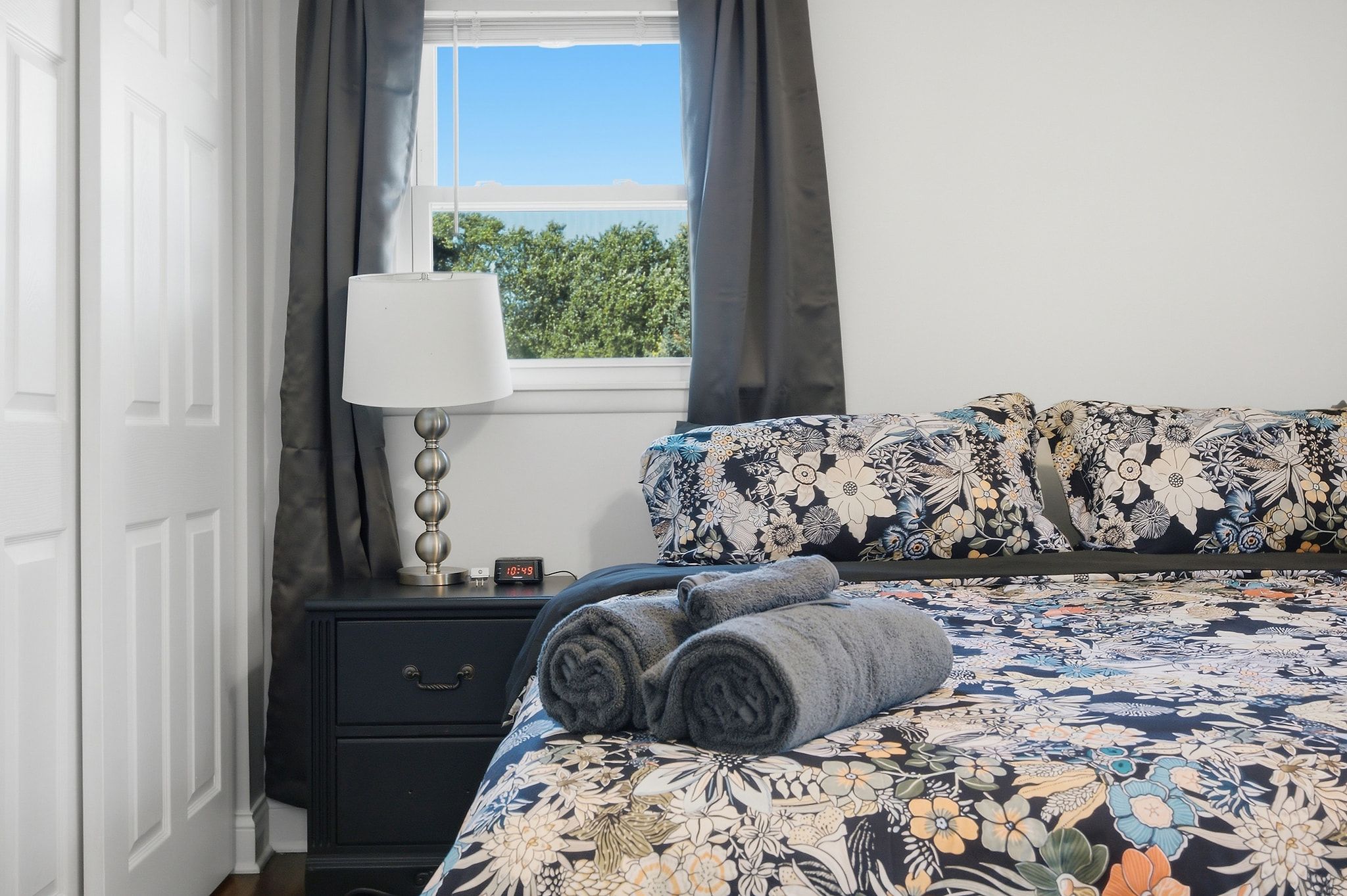 Une chambre à coucher avec un lit, une table de chevet avec une lampe, une horloge et une fenêtre avec des rideaux.
