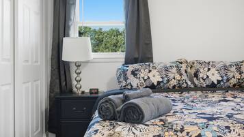 Une chambre à coucher avec un lit, une table de chevet avec une lampe, une horloge et une fenêtre avec des rideaux.
