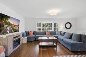 Een moderne woonkamer met een modulaire bank, een open haard en een groot raam met uitzicht op een brug en bomen.