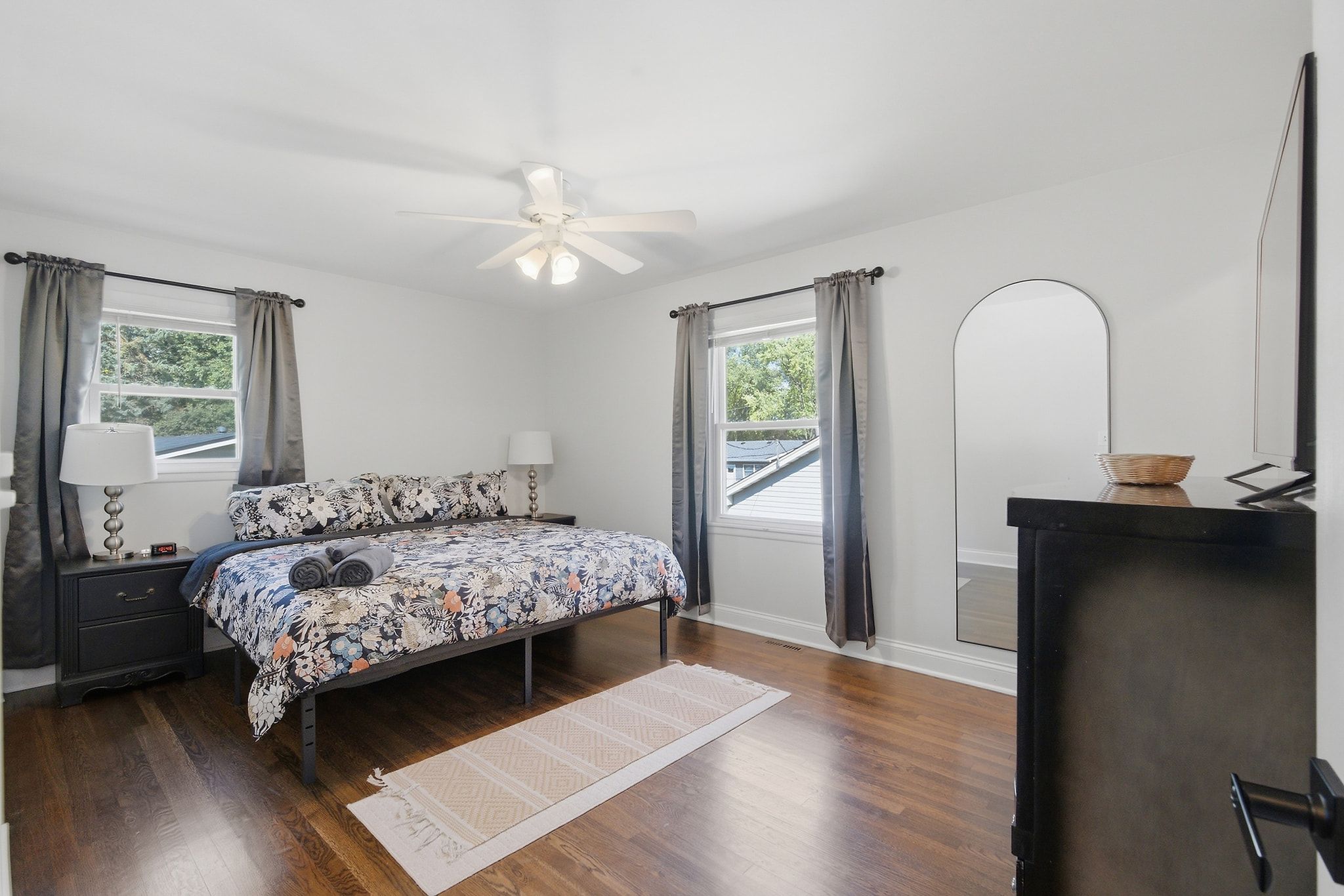 Une chambre à coucher comprenant un lit, des tables de chevet, un bureau, un ventilateur de plafond et une grande fenêtre.