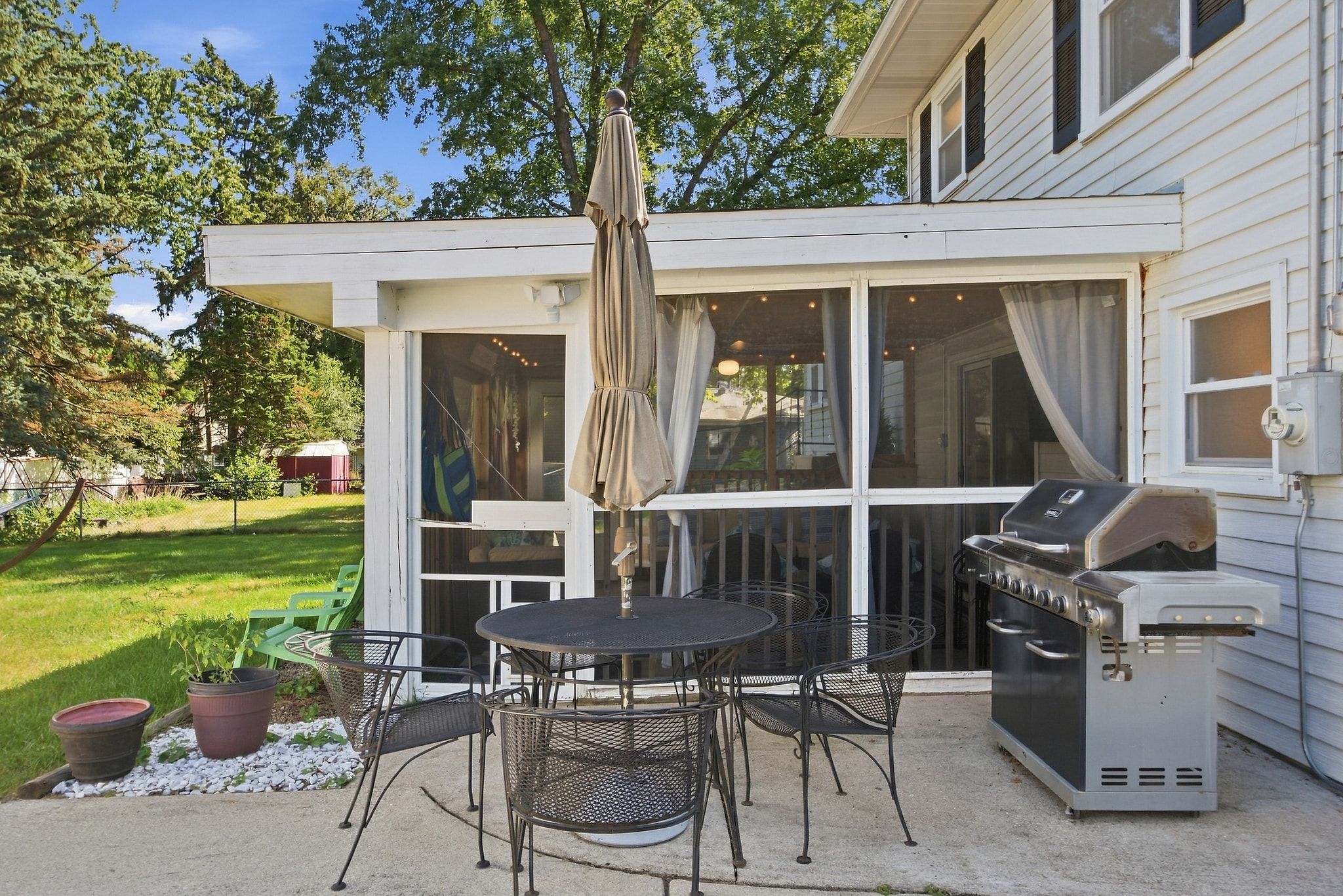Un patio couvert avec un barbecue, des sièges d’extérieur et une vue sur une maison.