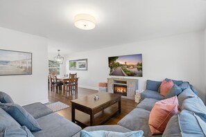 A living room with a fireplace, a dining area, and a sofa with cushions.