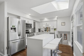 Una cocina moderna con electrodomésticos de acero inoxidable, una isla central con taburetes y un tragaluz.