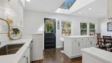 Une cuisine moderne avec des meubles blancs, un puits de lumière et une vue sur les arbres à l’extérieur.