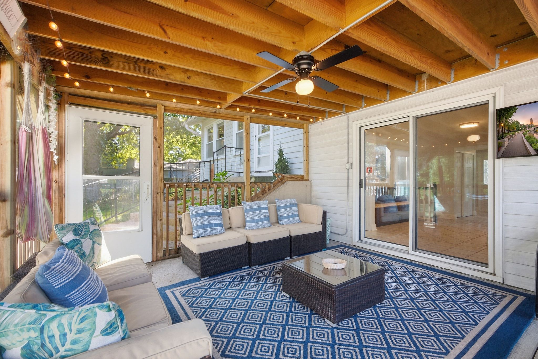 An outdoor patio with a ceiling fan, a sofa with cushions, a coffee table, and a patterned rug.