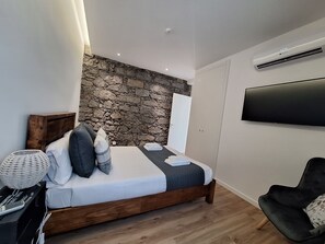Ein Schlafzimmer mit einer Wand aus Stein, einem Bett mit Kissen, einem Nachttisch mit Lampe und einem an der Wand befestigten Flachbildfernseher.