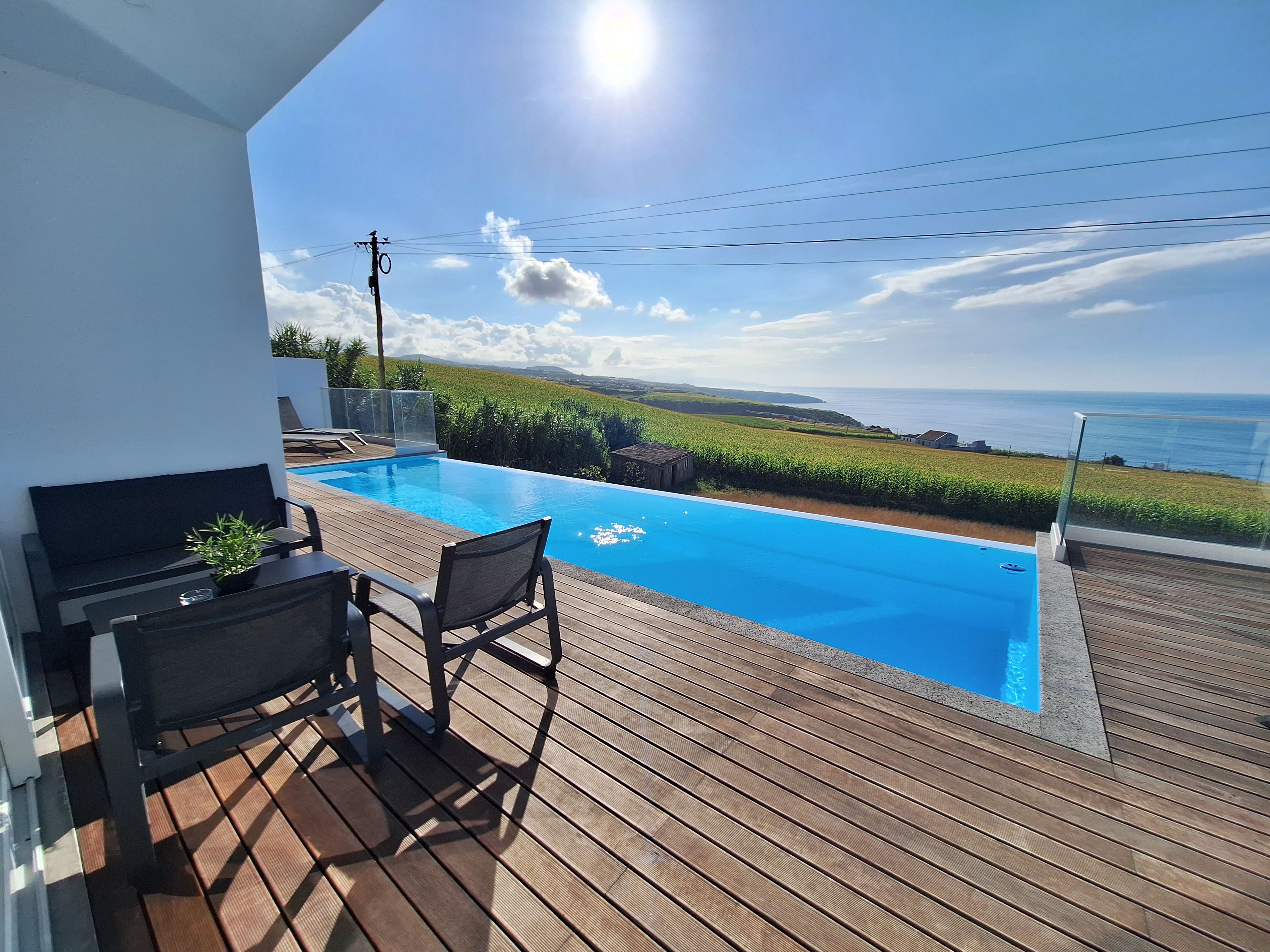 Una piscina con vista al mar, una terraza de madera y mobiliario exterior.
