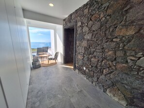 Ein modernes Interieur mit einer Steinwand, einer Essecke mit Tisch und Stühlen und Blick aufs Meer.