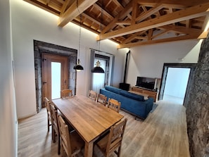Ein Essbereich mit Holztisch und Stühlen, einem blauen Sofa und einem Fernseher in einem modernen Wohnraum.