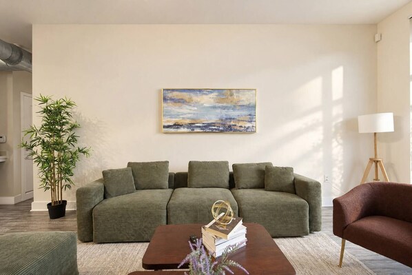 Ein Wohnzimmer mit einem grünen Sofa, einem Holztisch, einer Stehlampe und einem Gemälde an der Wand.
