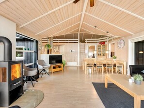 Een ruime woonkamer met houten plafond, een televisie, een open haard en een eethoek met stoelen en een tafel.