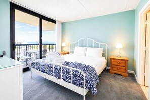 A hotel room with a bed, bedside tables, a desk, and a balcony with a view. - Sea Watch 119 (Ocean City)