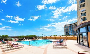 A swimming pool area with lounge chairs and a tall building in the background. - Sea Watch 119 (Ocean City)