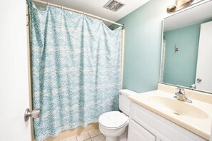 A bathroom with a shower curtain, toilet, sink, and mirror. - Sea Watch 119 (Ocean City)