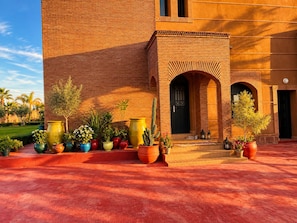 Un edificio con fachada de ladrillo, un patio con plantas en macetas y una puerta con un arco decorativo.