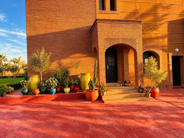 A building with a brick facade, a courtyard with potted plants, and a door with a decorative archway.