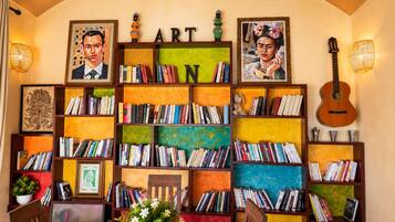 Een kamer met een boekenplank vol boeken, een gitaar en ingekaderde kunstwerken.