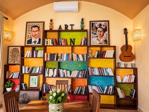 A room with a bookshelf filled with books, a guitar, and framed artwork.