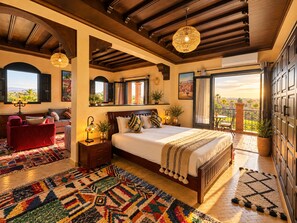 A bedroom with a large bed, a red sofa, a patterned rug, and a balcony with a view.