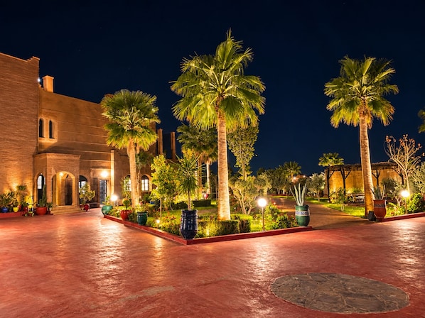 A courtyard with palm trees, a brick building, and a well-lit pathway.