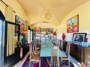Uma sala de jantar com uma mesa comprida, cadeiras e uma estante com diversos objetos.