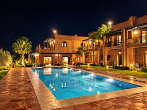 Un hotel de varios pisos con piscina, mobiliario exterior y palmeras.