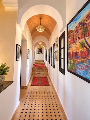A hallway with a tiled floor, a red carpet, and a painting on the wall.