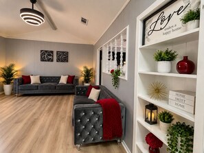 A modern living room with a grey sofa, a red throw blanket, and a white shelving unit with decorative items.