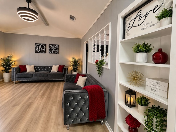 A modern living room with a grey sofa, a red throw blanket, and a white shelving unit with decorative items.
